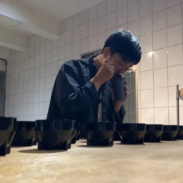 A brewer cups coffee behind a row of black ARC Dripper samples on a tasting table