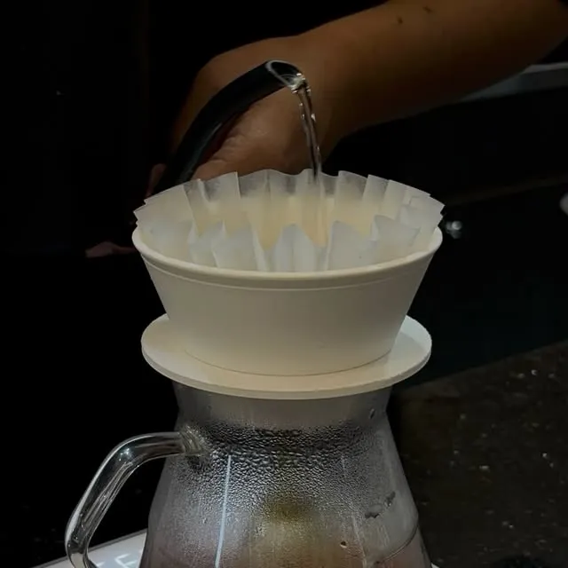 Water poured from a gooseneck kettle into a white ARC Dripper prototype with a wave filter