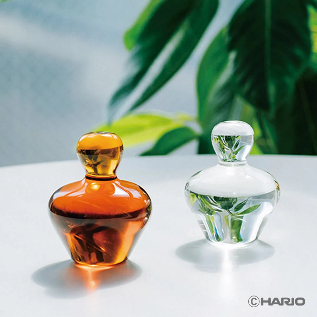 Amber and clear Glass Rinse Assist weights side by side on a white table, with a plant behind