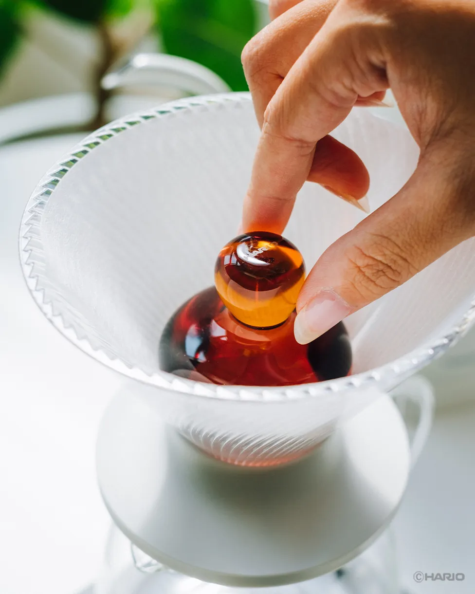 A hand lowering the amber Rinse Assist into a paper filter in a V60