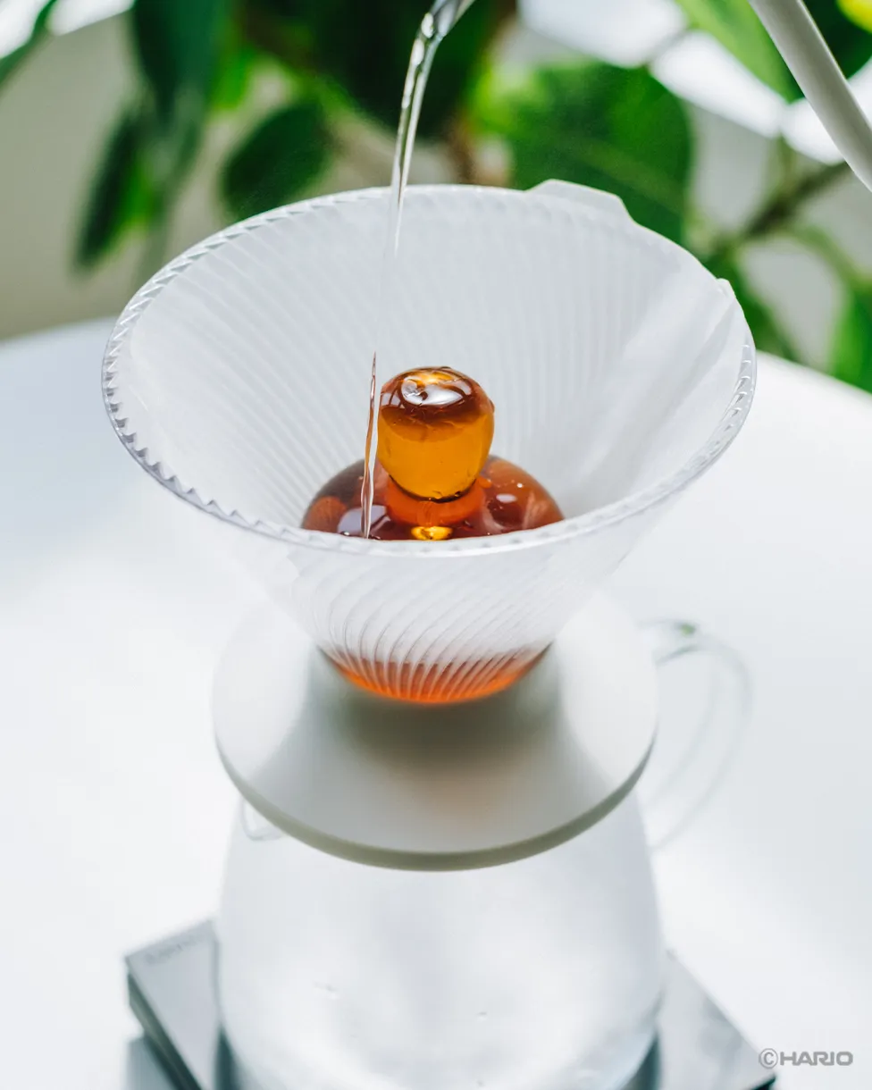 Water pouring over the amber Rinse Assist sitting in a paper-lined V60