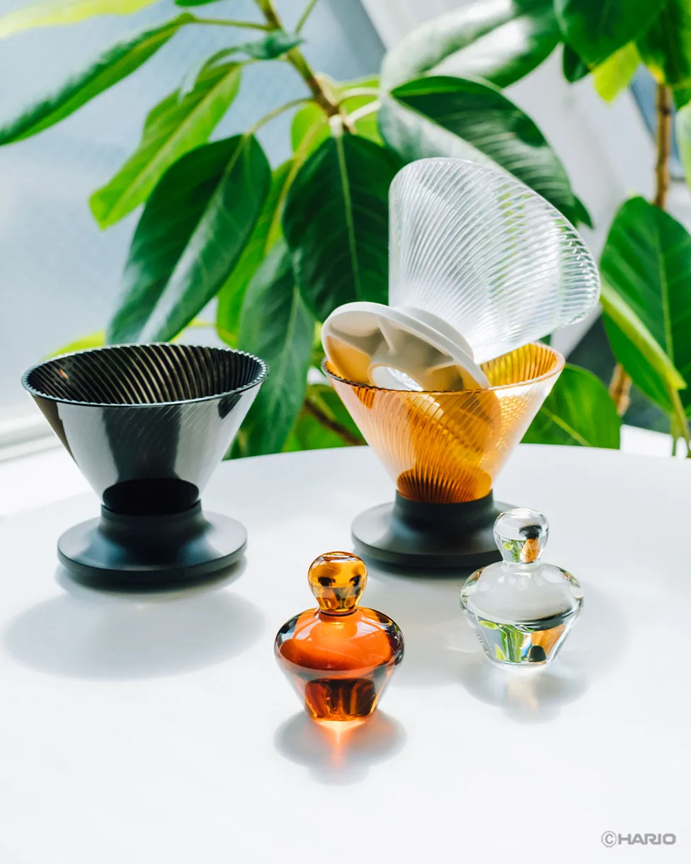 Amber and clear Rinse Assist weights in front of two ribbed glass drippers on black stands, one black and one amber