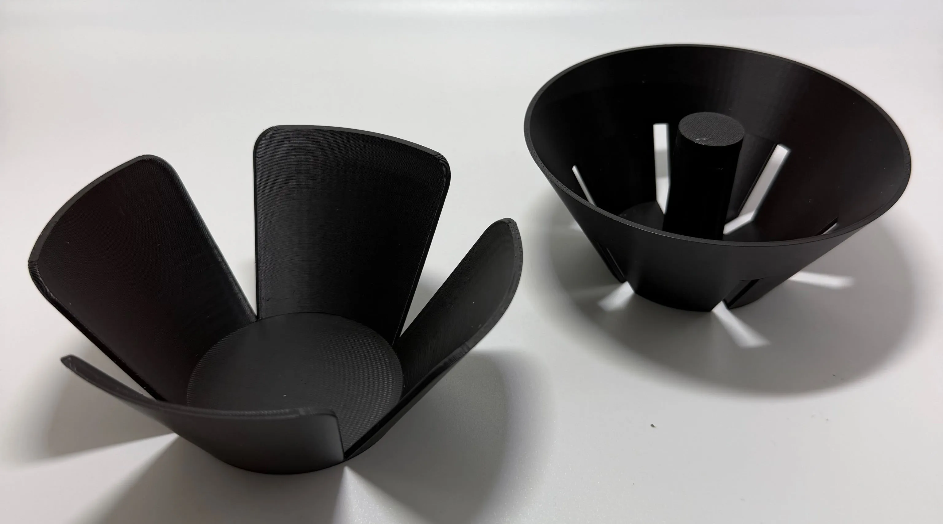 Black GX2 V2 dripper body with its central cone, next to the petal-shaped filter press used for flat-bottom papers