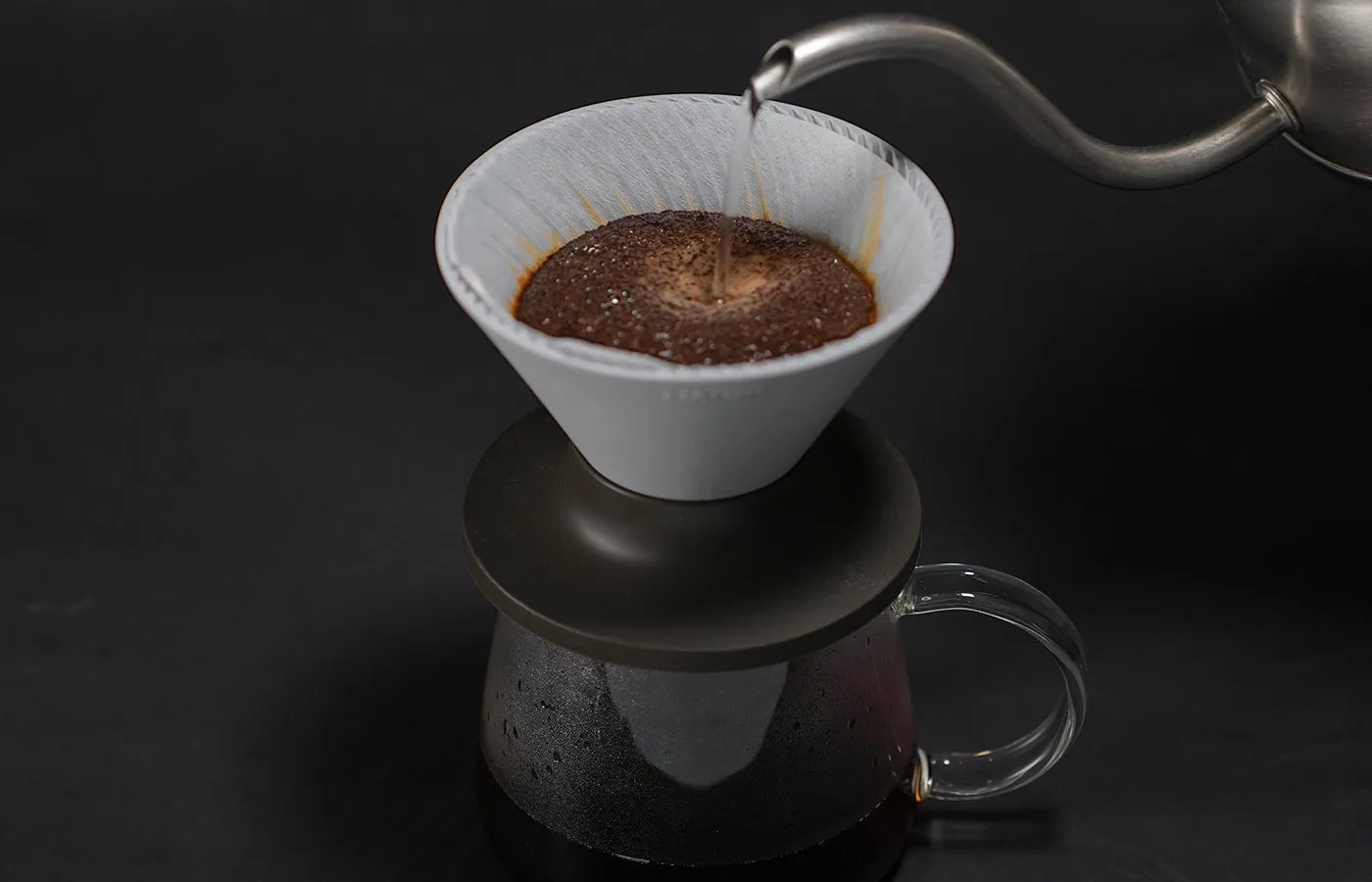Kettle pouring into a gray V60 NEO Ceramic dripper full of coffee grounds, on a glass server